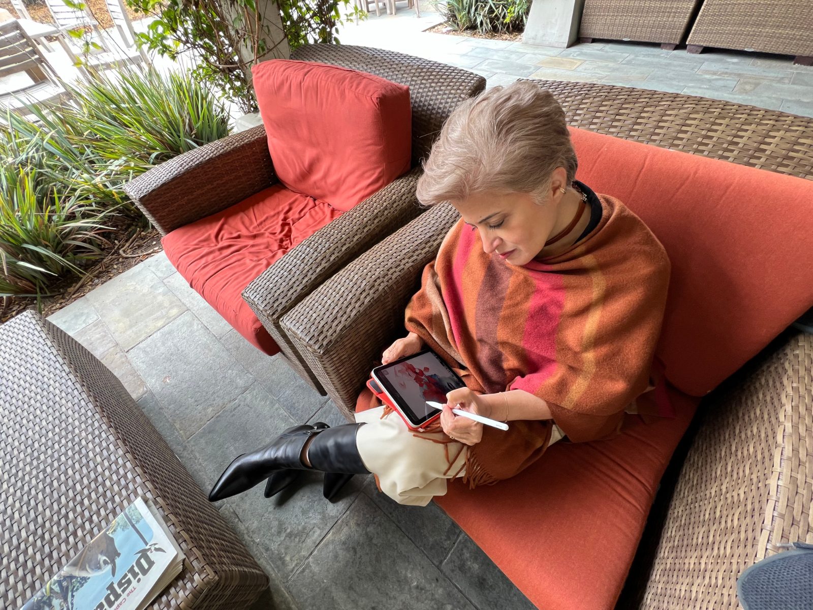 Aroosha writing on a tablet, wrapped in a warm shawl on a terracotta sofa