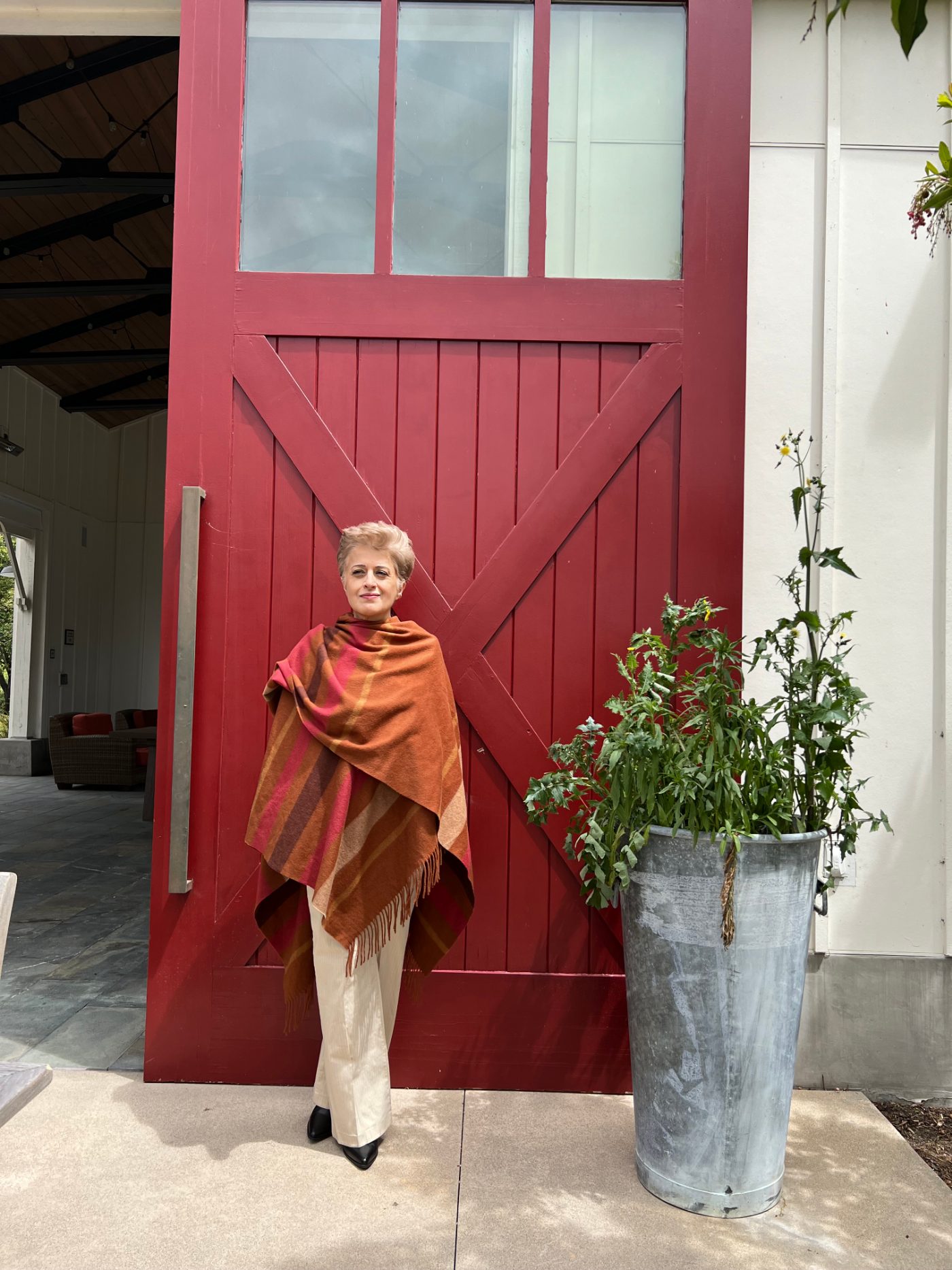 Aroosha standing in front of a red barn door, wearing a warm shawl
